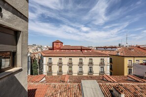Vista de tejados de tejas de terracota con un edificio que tiene varios balcones y un tejado rojo.