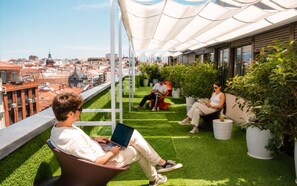 Une terrasse sur le toit, dotée d’un revêtement en gazon synthétique, d’espaces aménagés pour s’asseoir et de plantes en pot.
