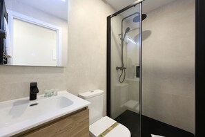 Un baño moderno con ducha acristalada, lavamanos blanco y retrete.