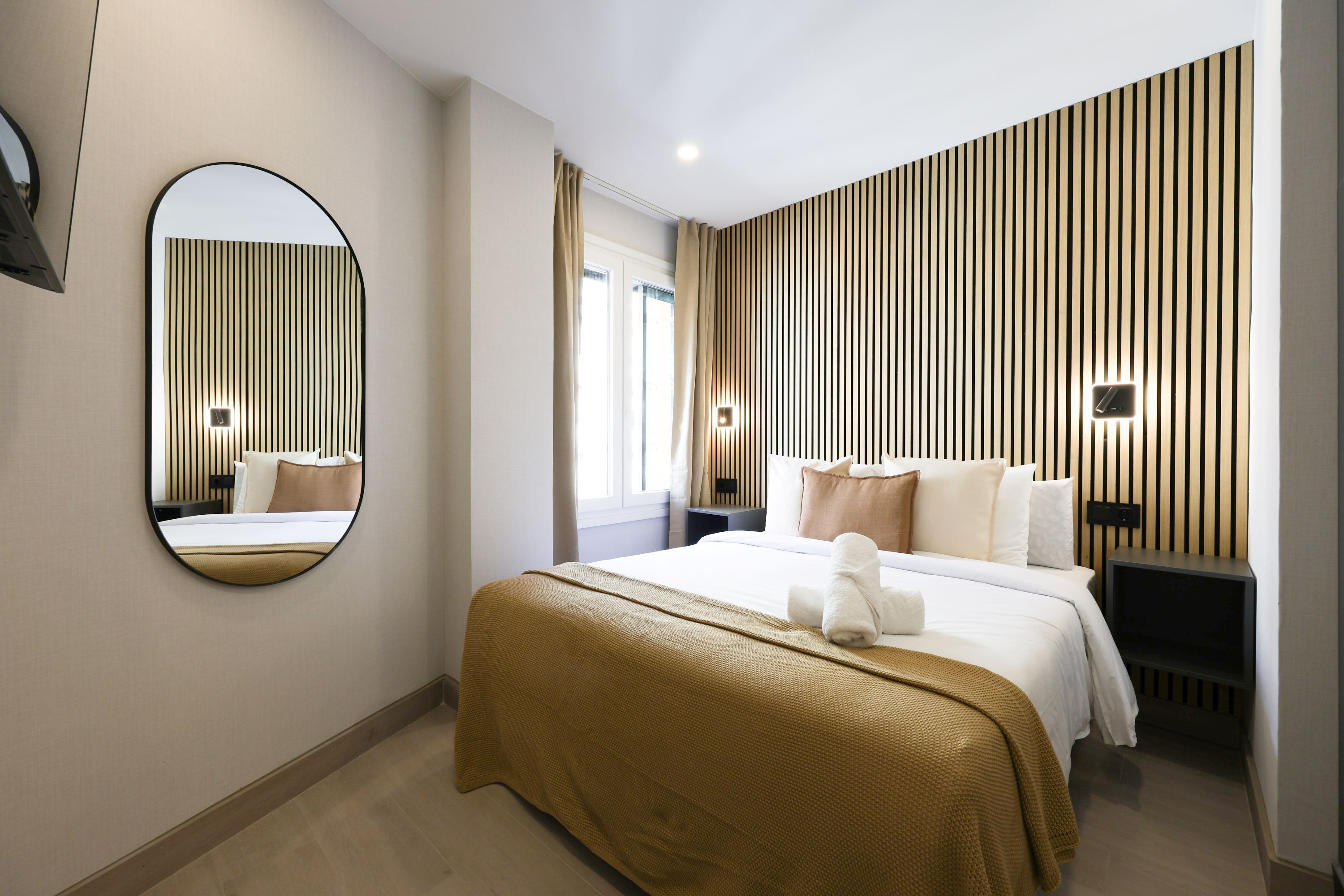 Ein Hotelzimmer mit einem großen Bett, einem runden Spiegel, einem Nachttisch und einer Wand mit vertikalen Holzlatten.
