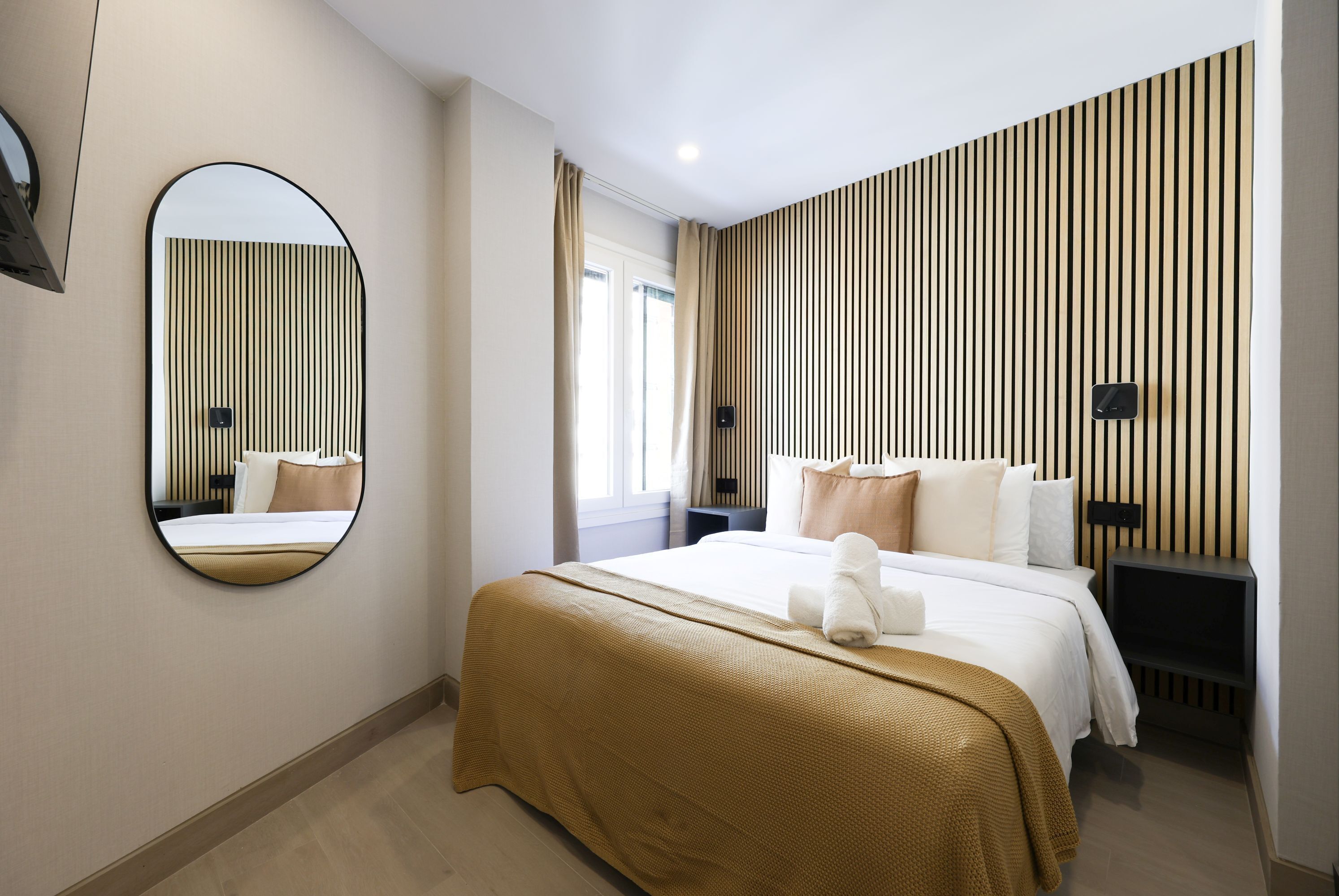 Een hotelkamer met een groot bed, een ronde spiegel, een nachtkastje en een aan de muur bevestigde televisie.