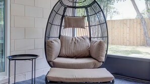 Zona salotto esterna moderna con una sedia in vimini circolare, un tavolino rotondo e vista sul giardino.