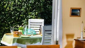 Een terras met rieten stoelen, een tafel voor twee en uitzicht op een weelderige groene haag.