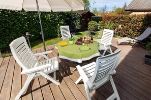Une terrasse avec une table ronde, des chaises blanches et une nappe verte.