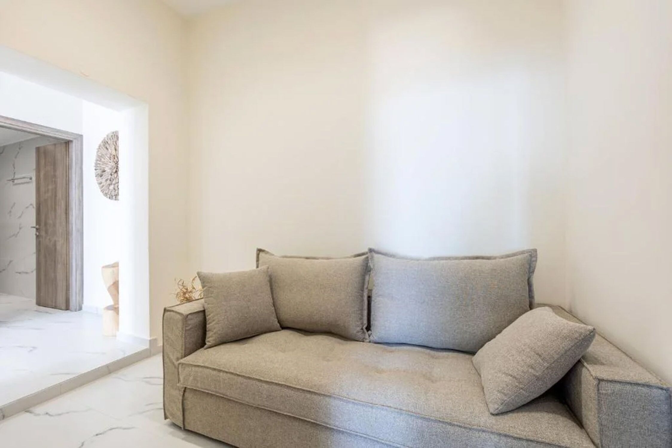 Een sofa in neutrale tinten in een hoek van een kamer met een marmeren vloer en een strak, modern design.