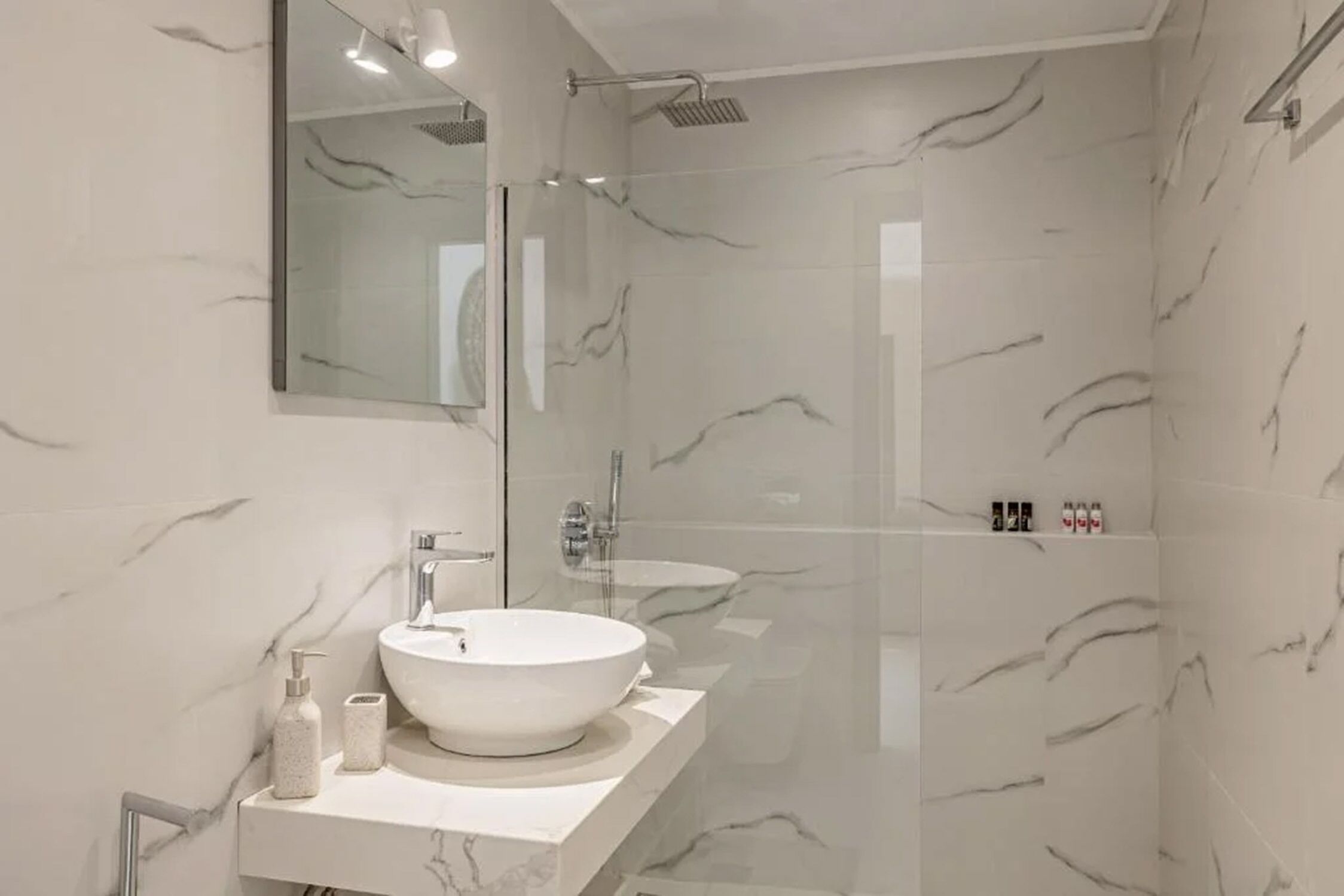 Une salle de bain moderne avec un grand miroir, un lavabo sur colonne blanc et une douche à parois de verre.