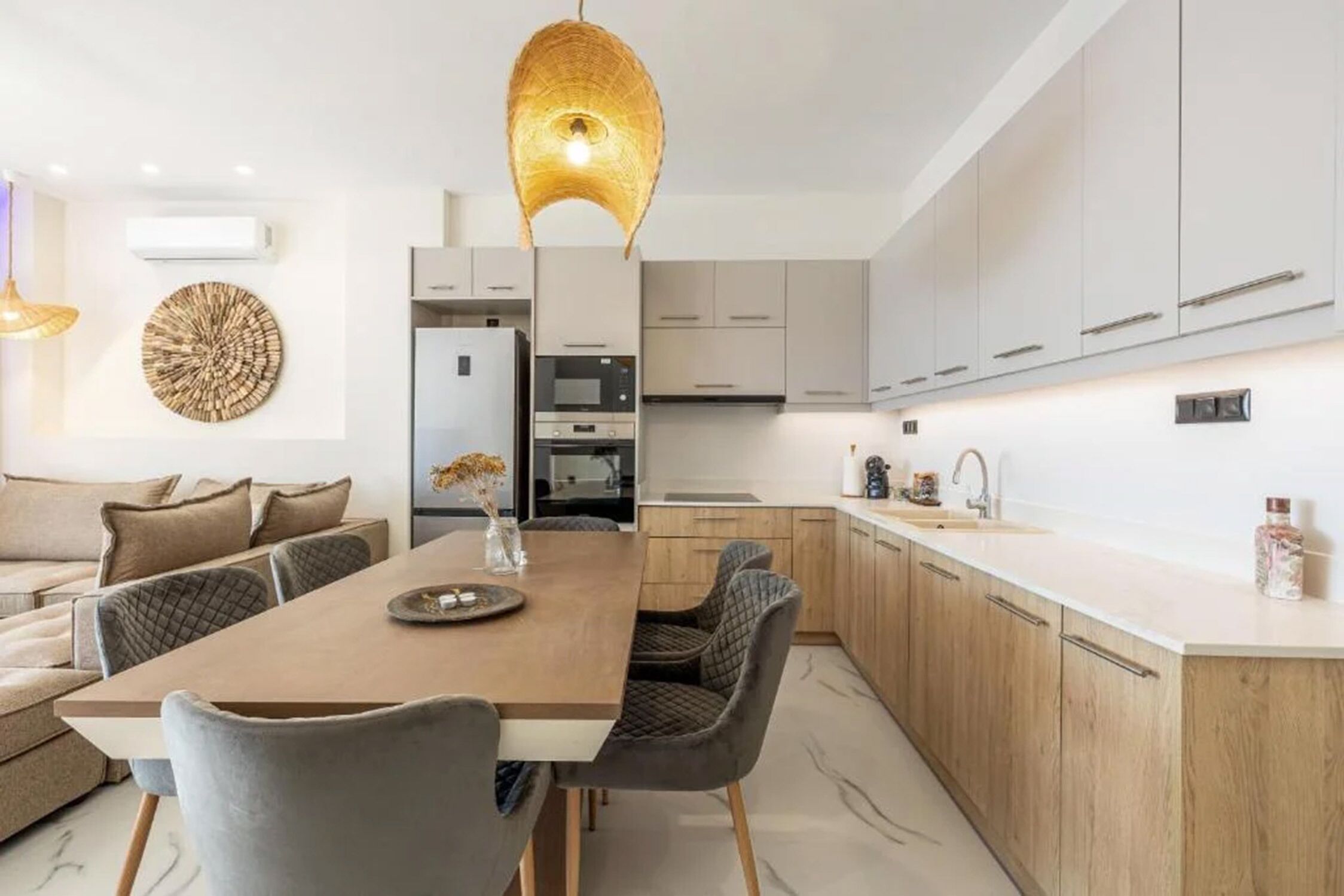 Een moderne keuken met een houten eettafel, grijs gestoffeerde stoelen en een hanglamp.