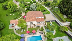 Uma casa grande com piscina, cercada por gramados bem cuidados e árvores.