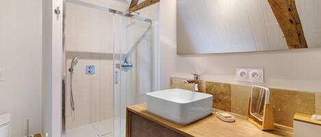 Une salle de bain avec une douche à parois de verre, un lavabo blanc, un meuble-lavabo en bois et un grand miroir.
