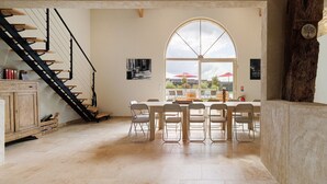 Um quarto amplo com uma mesa de jantar, cadeiras, uma escada e uma grande janela em arco.