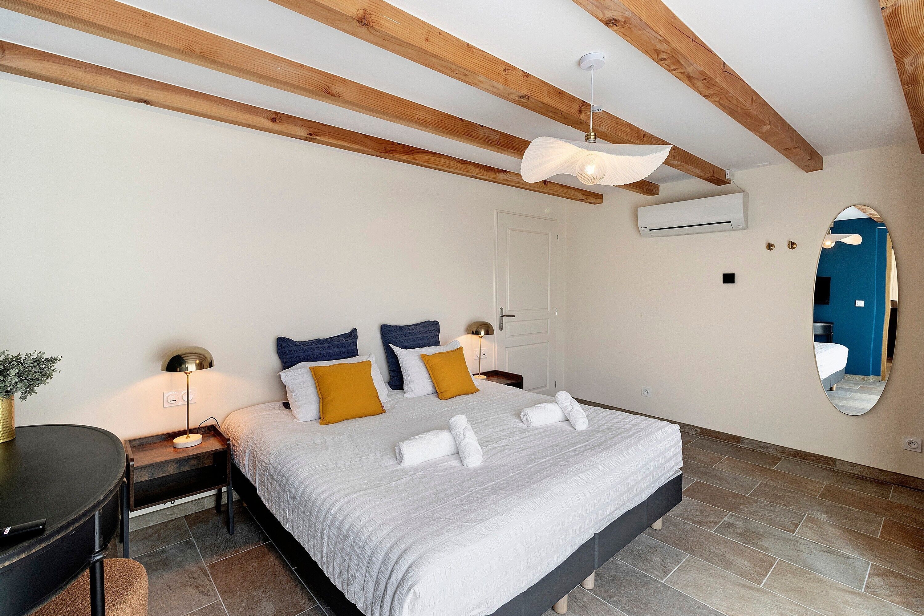 Een slaapkamer met een bed, nachtkastjes, een bureau, een spiegel en een airconditioning.