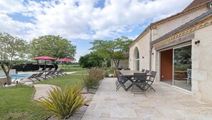 Une terrasse avec une table et des chaises, une piscine et un bâtiment à la façade en pierre.