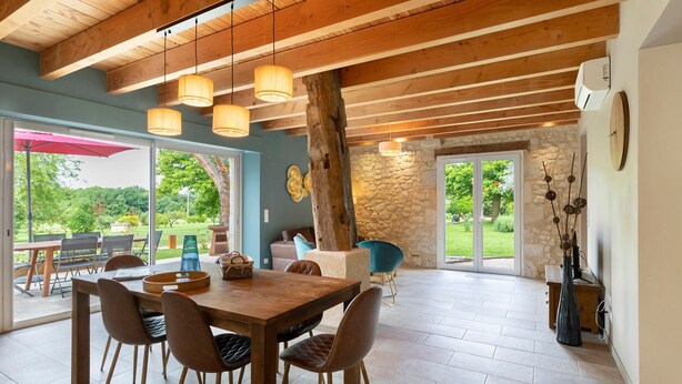 Un espace repas avec une table et des chaises en bois, un mur en pierre et une vue sur l’extérieur.