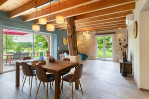 A dining area with a wooden table and chairs, a stone wall, and a view of the outdoors. - Gîte Les Lilas - Les Carassonnes with Shared Pool, Wi-Fi, and Air Conditioning (Saint-Nexans)
