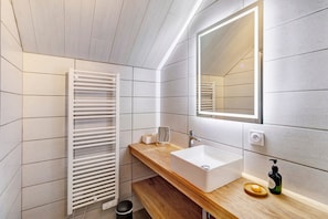 A modern bathroom with a wooden vanity, white sink, and a towel rack. - Gîte Les Lilas - Les Carassonnes with Shared Pool, Wi-Fi, and Air Conditioning (Saint-Nexans)