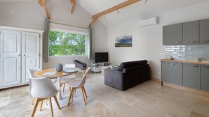 A modern kitchen with grey cabinets, a dining area with a round table and chairs, and a grey sofa. - Gîte L'albizia - Les Carassonnes with Shared Pool, Wi-Fi and Air Conditioning (Saint-Nexans)