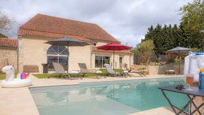 A poolside area with lounge chairs, umbrellas, and a stone building with a tiled roof. - Gîte L'albizia - Les Carassonnes with Shared Pool, Wi-Fi and Air Conditioning (Saint-Nexans)