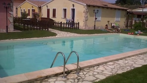 Piscina com azulejos de pedra e grades de metal, cercada por uma área gramada e uma cerca de madeira.