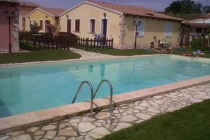 A swimming pool with stone tiles and metal railings, surrounded by a grassy area and a wooden fence. - Relaxing Flat With Shared Pool in Viddalba (Viddalba)