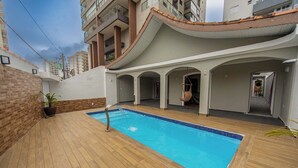 Una piscina sul tetto con pavimento in legno e acqua blu cristallina, circondata da un edificio bianco con un tetto curvo e numerosi balconi.