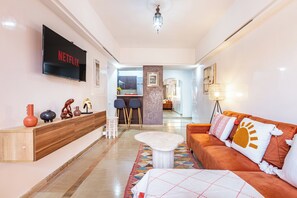 A modern living room with a flat-screen TV, a wooden console table, a sofa with patterned cushions, and a dining area in the background. - Chic and cozy apartment in the heart of Guéliz - Orienthai (Marrakech)