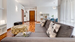 Moderni olohuone, jossa on sohva, rahi ja taustalla ruokailutila.