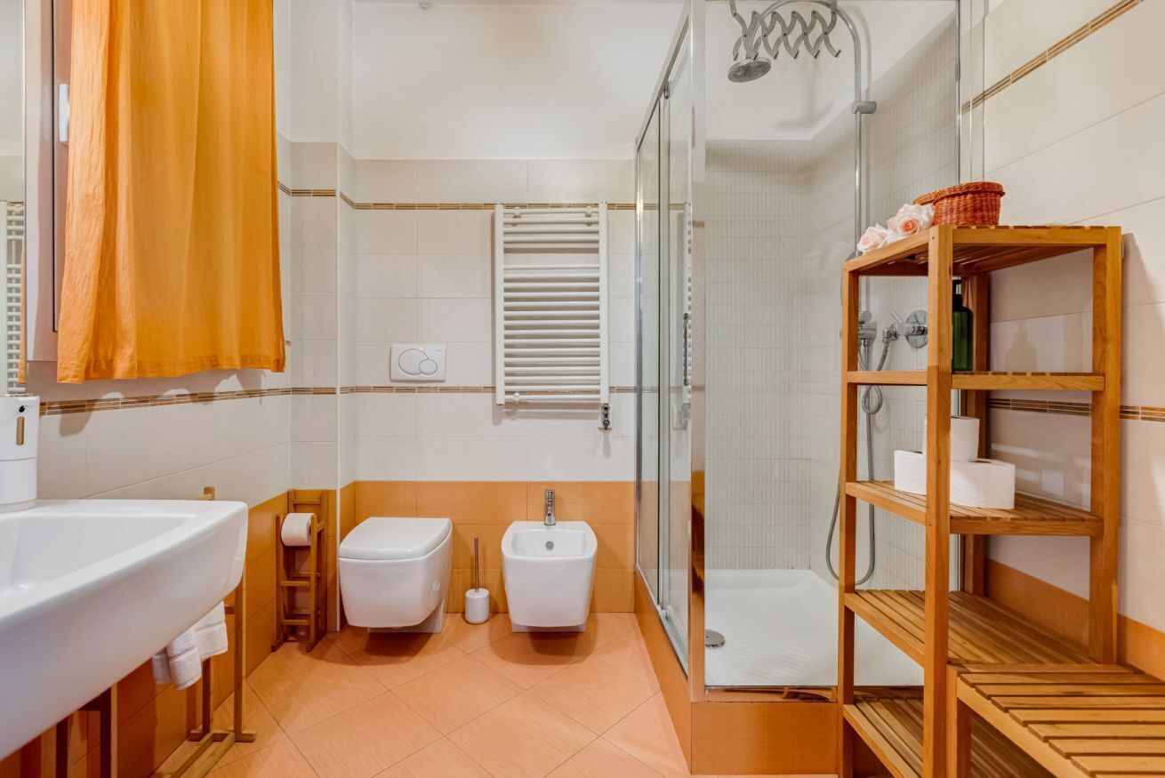 Bany amb rentamig, vàter, bidet, dutxa i prestatges de fusta.
