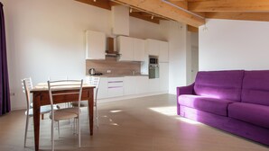 Une cuisine moderne avec des meubles blancs, une table à manger en bois et un canapé violet.