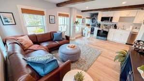 A modern living room with a brown leather sofa, a round coffee table, and a kitchen in the background. - Charming 2BR•Walk to Harbor & Downtown•Close2Salem (Gloucester)