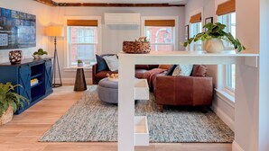 A modern living room with a brown leather sofa, a blue cabinet, and a large TV on the wall. - Charming 2BR•Walk to Harbor & Downtown•Close2Salem (Gloucester)