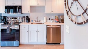 A modern kitchen with white cabinets, stainless steel appliances, and a large wall clock. - Charming 2BR•Walk to Harbor & Downtown•Close2Salem (Gloucester)