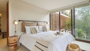Ein modernes Schlafzimmer mit einem großen Bett, Nachttischen, Blick ins Freie und einem Holzkopfstück.