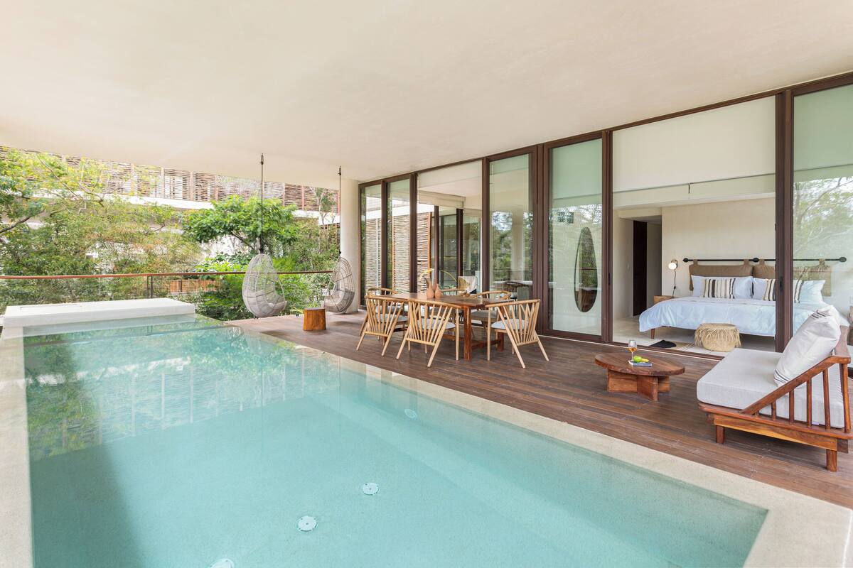 A modern outdoor pool area with a wooden deck, a dining set, and a lounge chair.