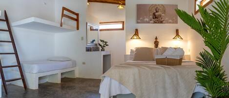 Ein Schlafzimmer mit Etagenbett, Nachttisch mit Lampe, kleinem Schreibtisch, Stuhl und einer großen Pflanze.