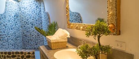 Une salle de bain avec un mur en pierre, un lavabo, un miroir, un panier en osier contenant une serviette et une plante en pot.