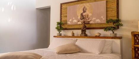 A bedroom with a bed, pillows, a Buddha statue, and a painting on the wall.