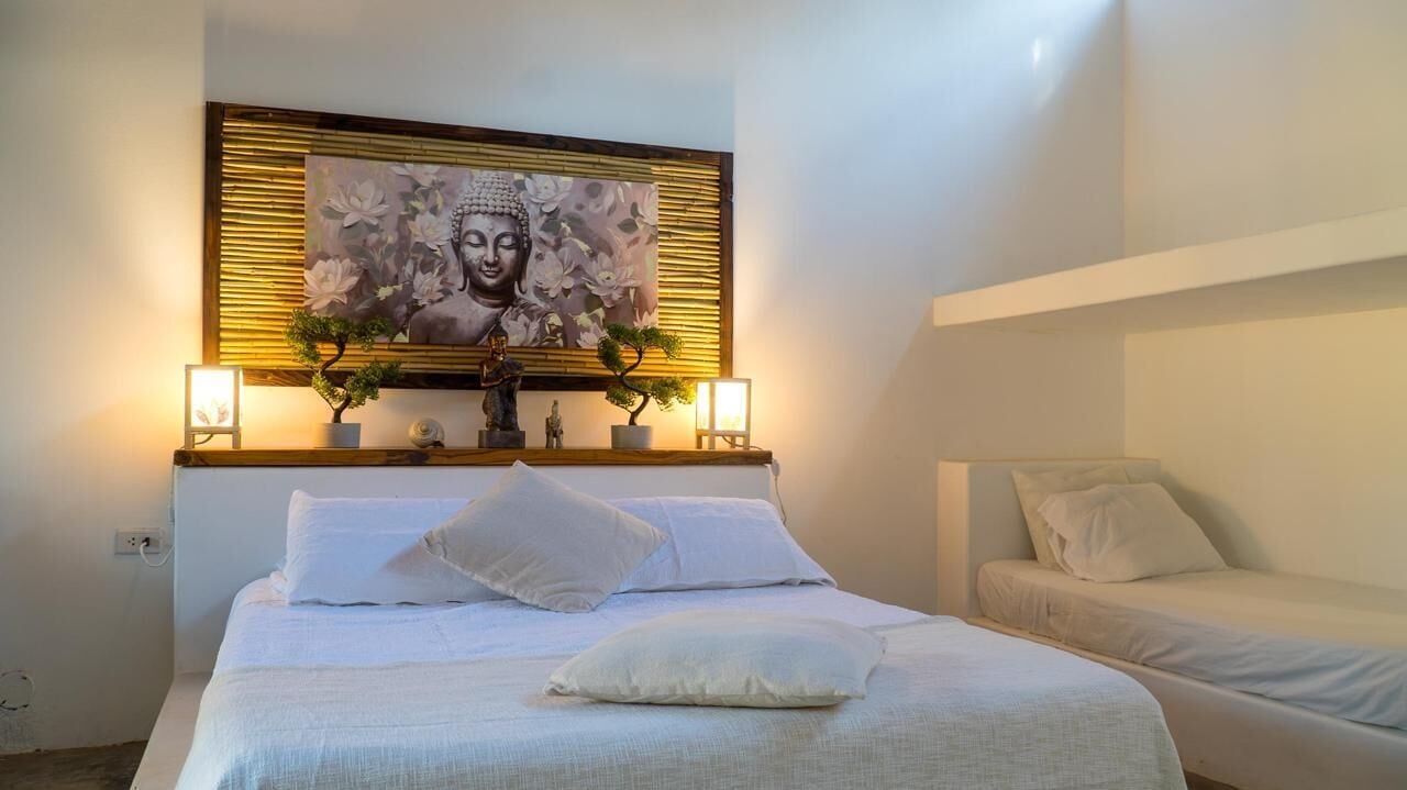 A bedroom with a large bed, a smaller bed, a wall-mounted Buddha painting, and a small Buddha statue on a shelf.