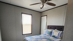Un dormitorio con cama, ventilador de techo, ventana con persianas y suelo de madera.