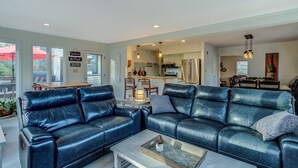 Ein modernes Wohnzimmer mit einer schwarzen Ledersofa, einem Holztisch und Blick auf die Küche und den Essbereich.