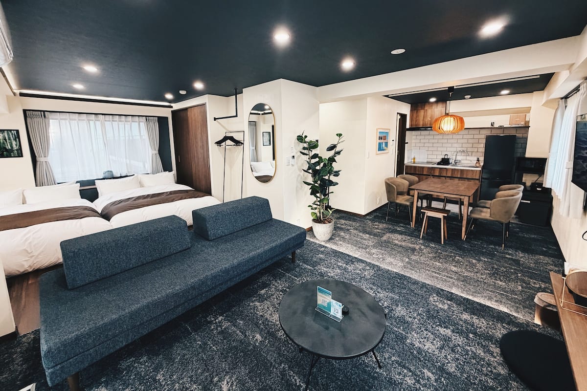 Una habitación de hotel moderna con cama, sofá, mesa de comedor y área de cocina.