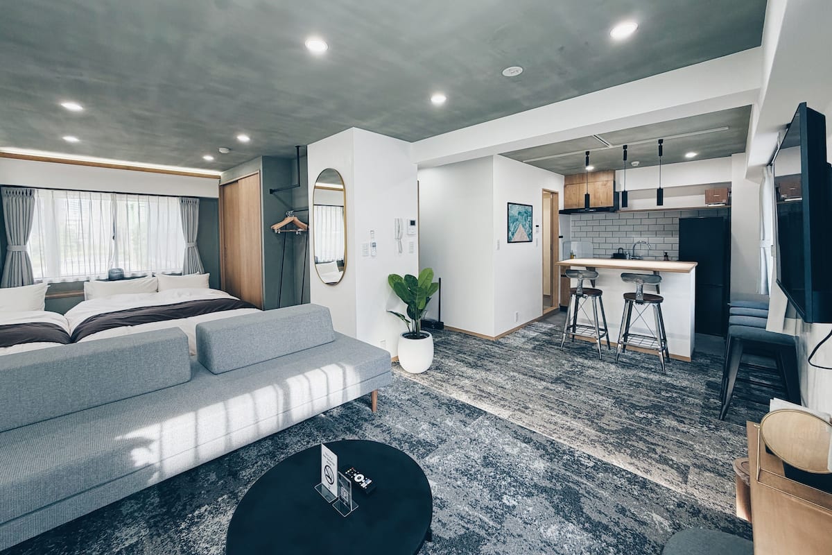 Una habitación de hotel moderna con una cama grande, un sofá, una pequeña mesa de centro y una zona de cocina con barra.