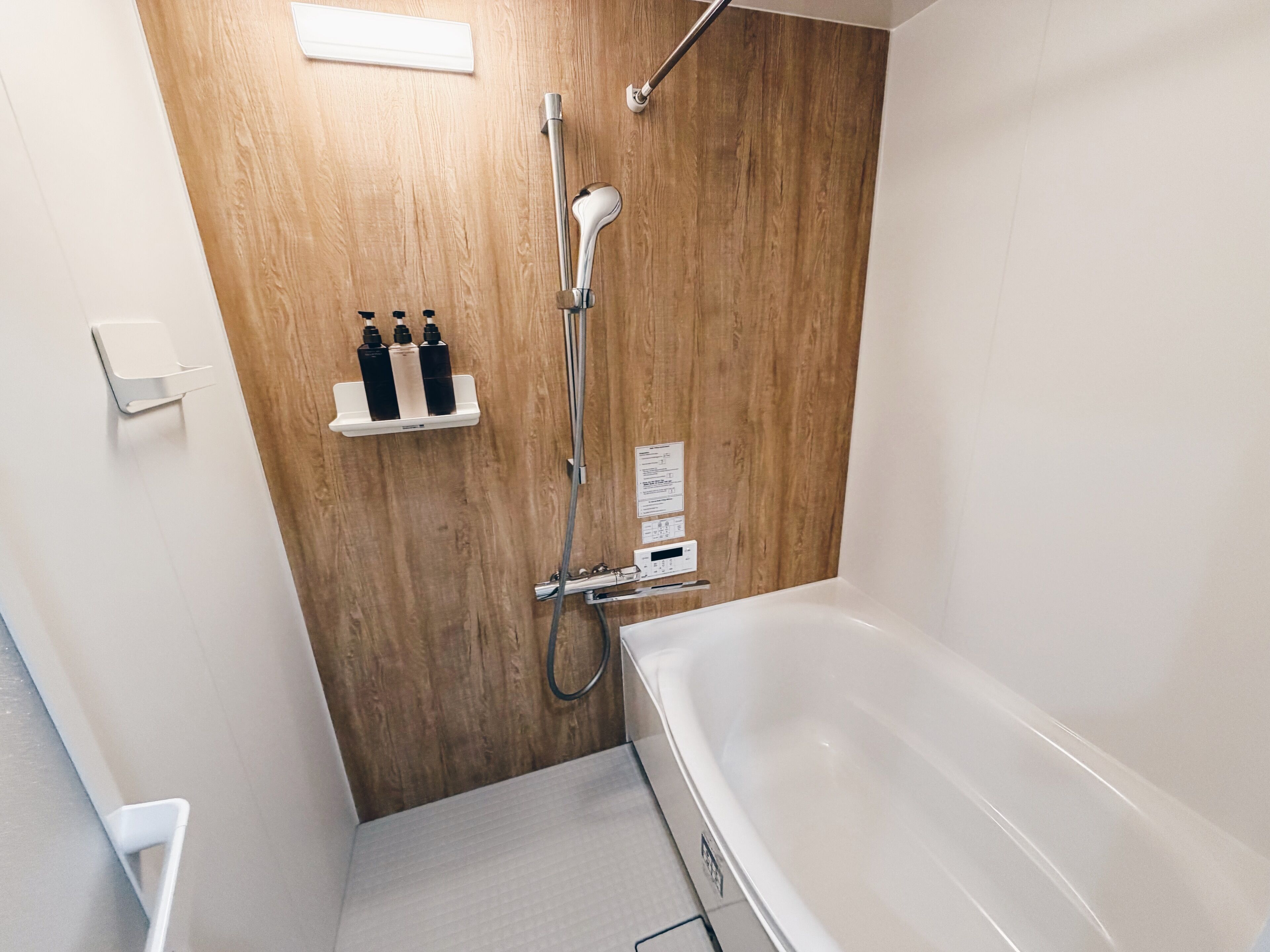 A modern bathroom with a wooden wall, a white bathtub, and a shower area.
