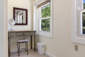 A bathroom with a vanity, a mirror, a chair, and a trash bin.