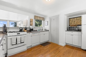 A modern kitchen with white cabinetry, a gas stove, a microwave, and a coffee maker. - Lupine Cottage | Walk to Downtown Rockland Harbor (Owls Head)