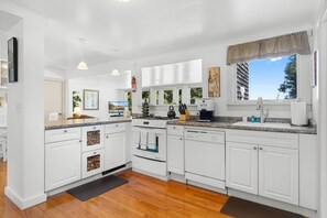 A modern kitchen with white cabinetry, a built-in oven, a dishwasher, and a large window with a view of the outdoors.