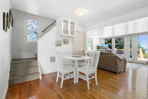 A modern interior with a staircase, dining area, and a sofa facing large windows. - Lupine Cottage | Walk to Downtown Rockland Harbor (Owls Head)