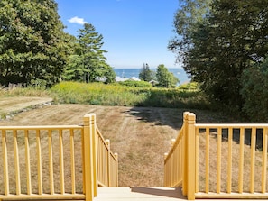 A wooden staircase leading to a grassy area with a view of the ocean and boats in the distance. - Lupine Cottage | Walk to Downtown Rockland Harbor (Owls Head)