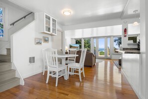 A spacious living area with a dining table and chairs, a staircase, and a view of the outdoors.
