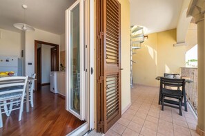 A spacious living area with a sliding glass door leading to a balcony, a dining table with chairs, and a kitchen area with a refrigerator and cabinets. - Panoramic sea View Apartment in Porto Torres (Porto Torres)