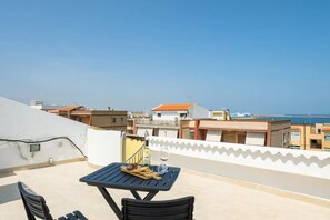 A rooftop terrace with a table and chairs, overlooking a coastal area with buildings and a clear sky. - Panoramic sea View Apartment in Porto Torres (Porto Torres)
